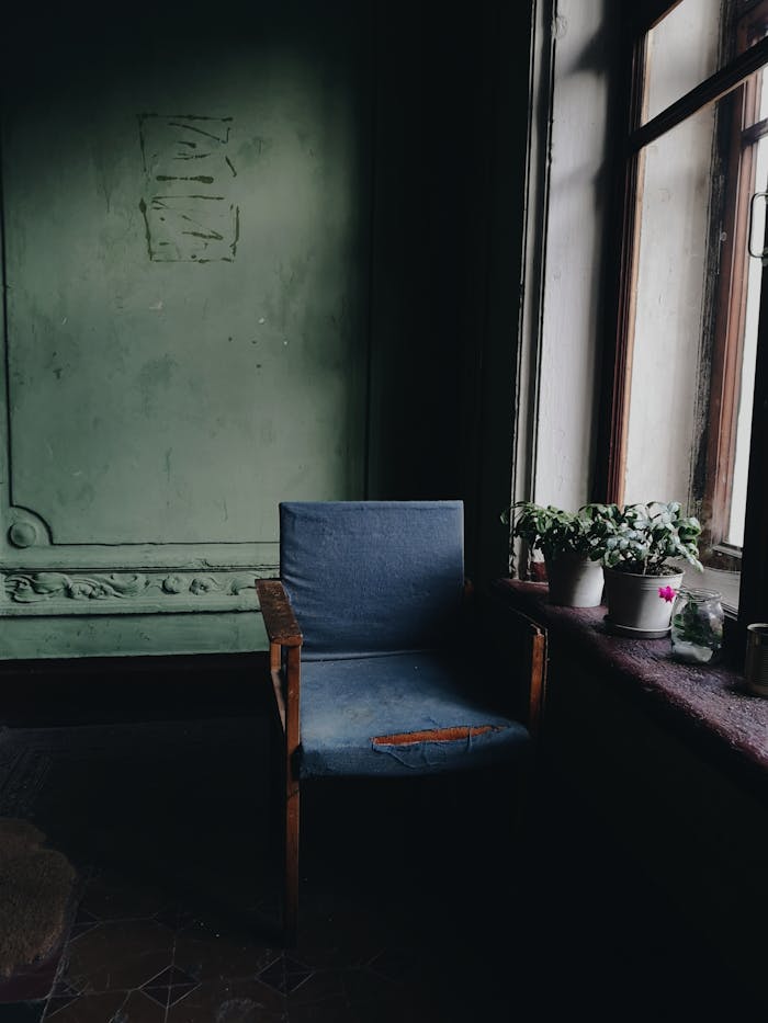 A quiet and cozy vintage chair sits by a sunlit window in a rustic room, creating a serene interior atmosphere.
